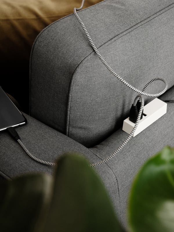 A LÖRBY magnetic USB charger on the back of a grey sofa with two charging cables attached to it, one going to a mobile phone.