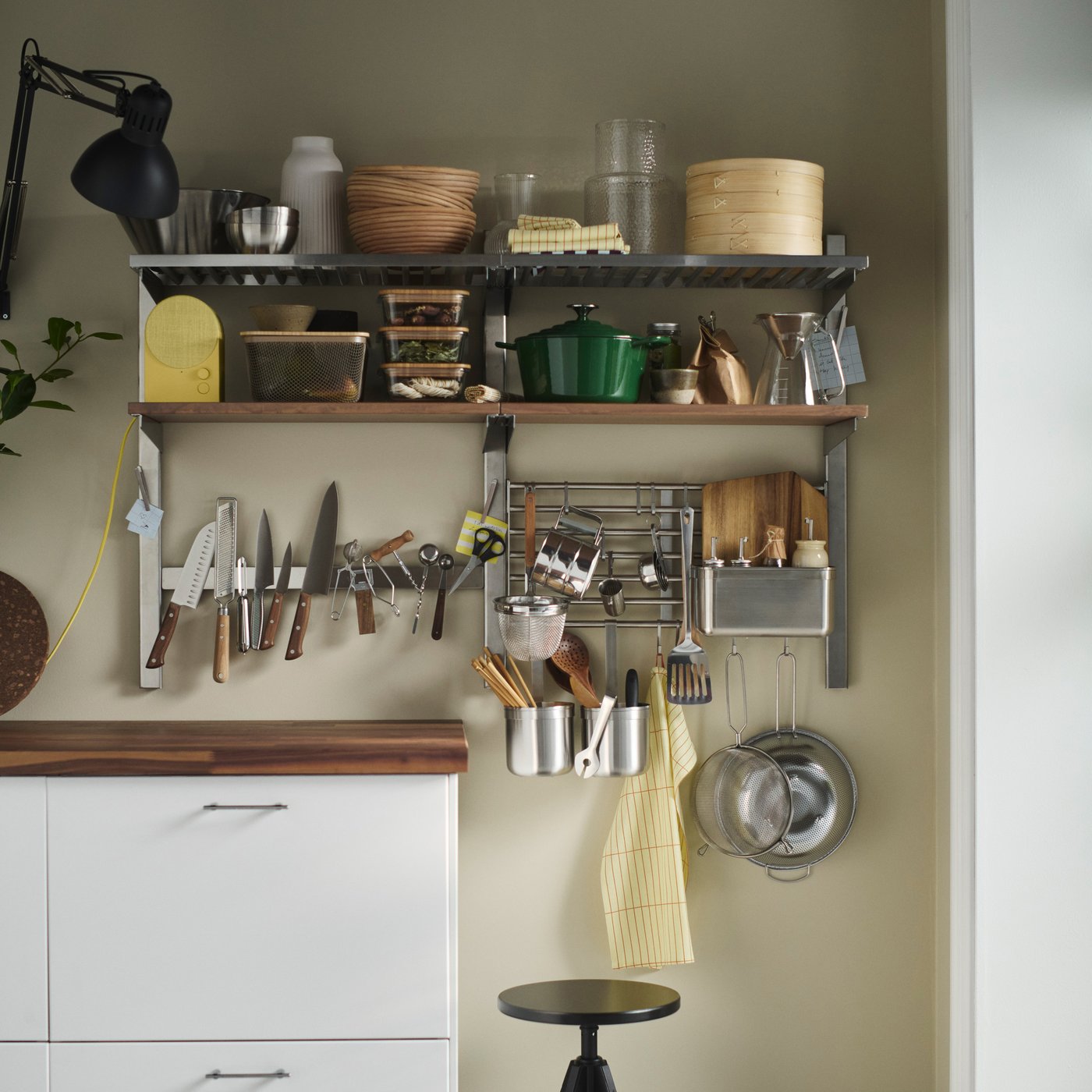 A kitchen wall fitted with open shelves, rails and a magnetic knife rack which are all packed with everyday kitchen items.