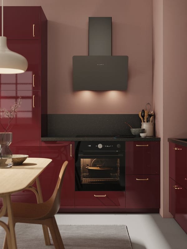METOD kitchen system with KALLARP high gloss dark red doors showing a oven switched on and baking a pie.