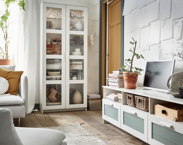 Una vitrina blanca BRIMNES al costado de un mueble para TV en una sala.