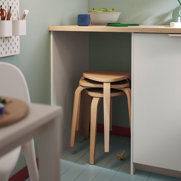 Uno sgabello KYRRE in legno chiaro sotto un tavolo in una cucina luminosa con una ciotola di frutta.