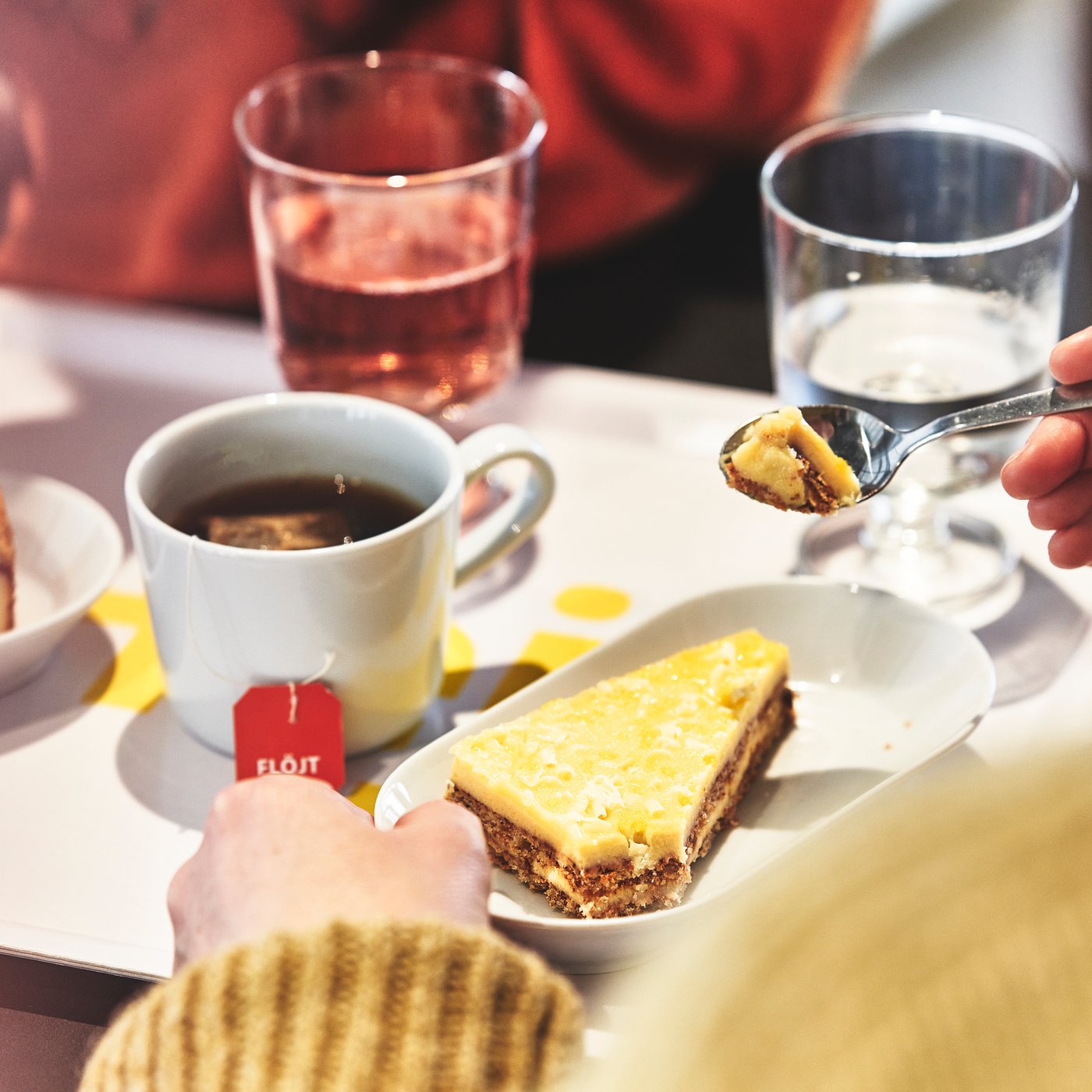 Alcune persone sedute a tavola con bevande in tazze e bicchieri e una fetta di torta svedese al limone.