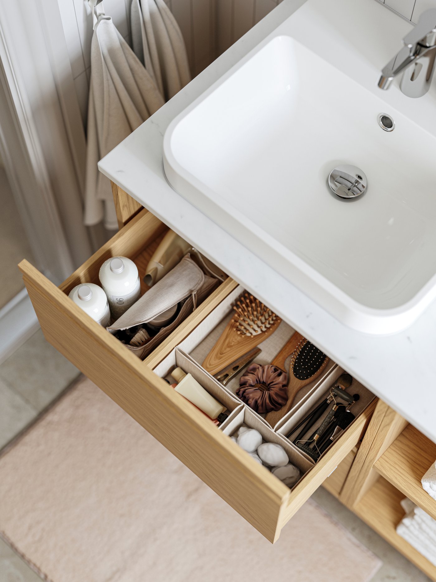 Un meuble-lavabo ÄNGSJÖN à tiroirs a un tiroir tiré et des accessoires de rangement pour tiroirs BOLLÖSUND beiges à l’intérieur.