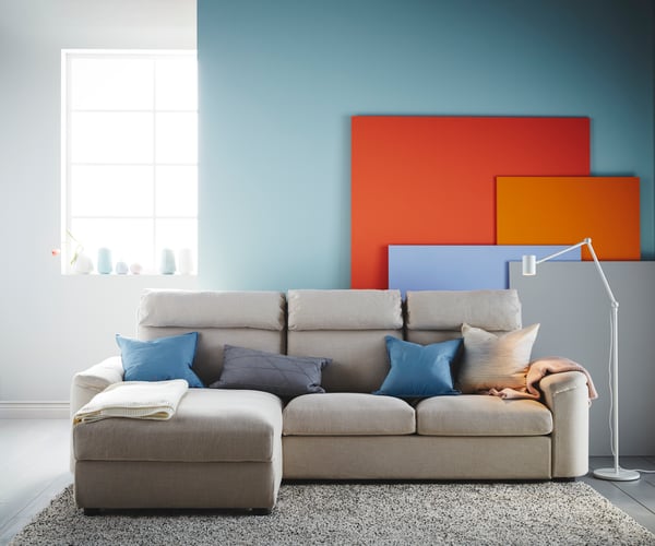 A grey sofa in front of a light blue wall in the living room, with several colourful panels in orange, red, blue and grey.