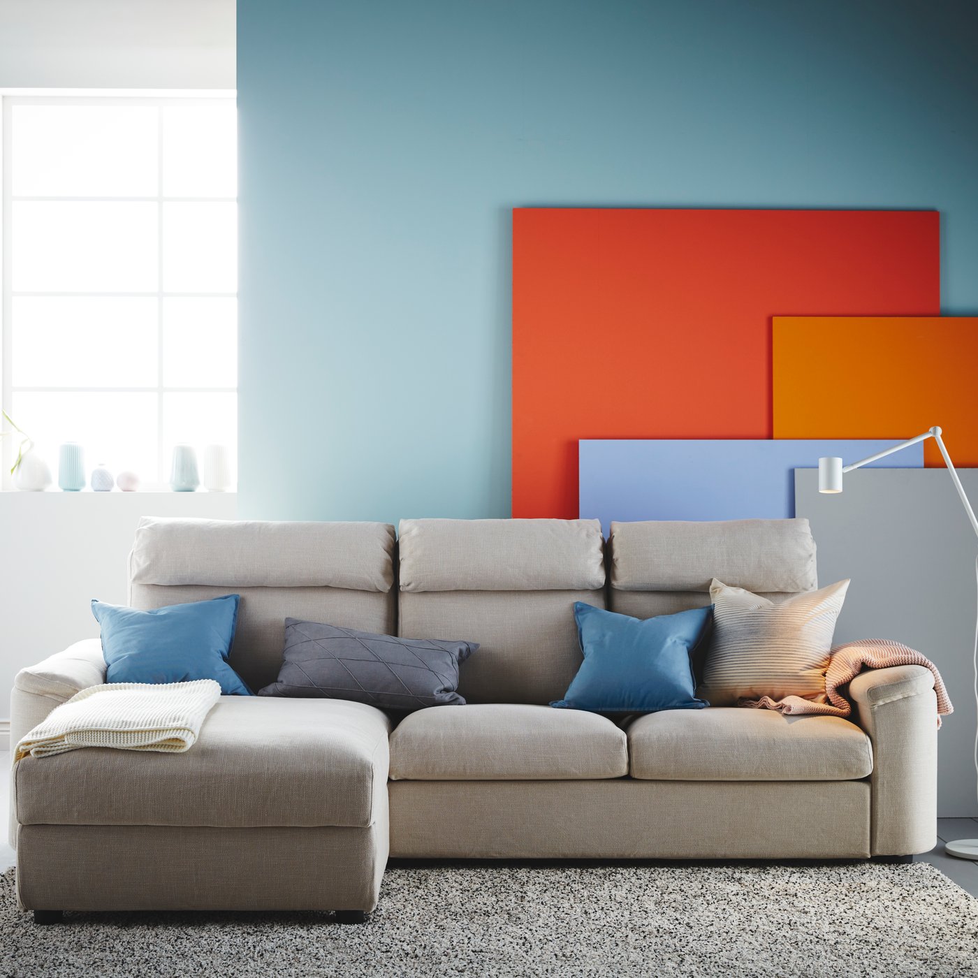A grey sofa in front of a light blue wall in the living room, with several colourful panels in orange, red, blue and grey.