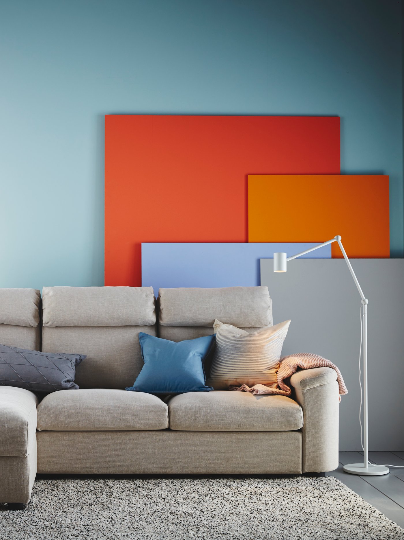 A grey sofa stands in front of a light blue wall in the living room, with various coloured panels in orange, red, blue and grey.