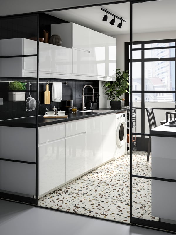 A kitchen with a sink and a washing machine in the colors white and black.