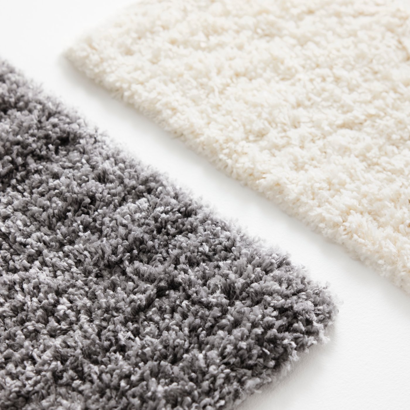 A close-up of the thick, soft pile of two ÄRENDE rugs, one in grey and one in off-white.