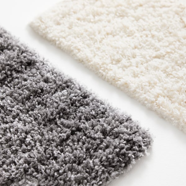 A close-up of the thick, soft pile of two ÄRENDE rugs, one in grey and one in off-white.