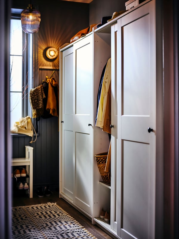 Two white HAUGA wardrobes with sliding doors partially open revealing the arms of a few items of hanging clothing.