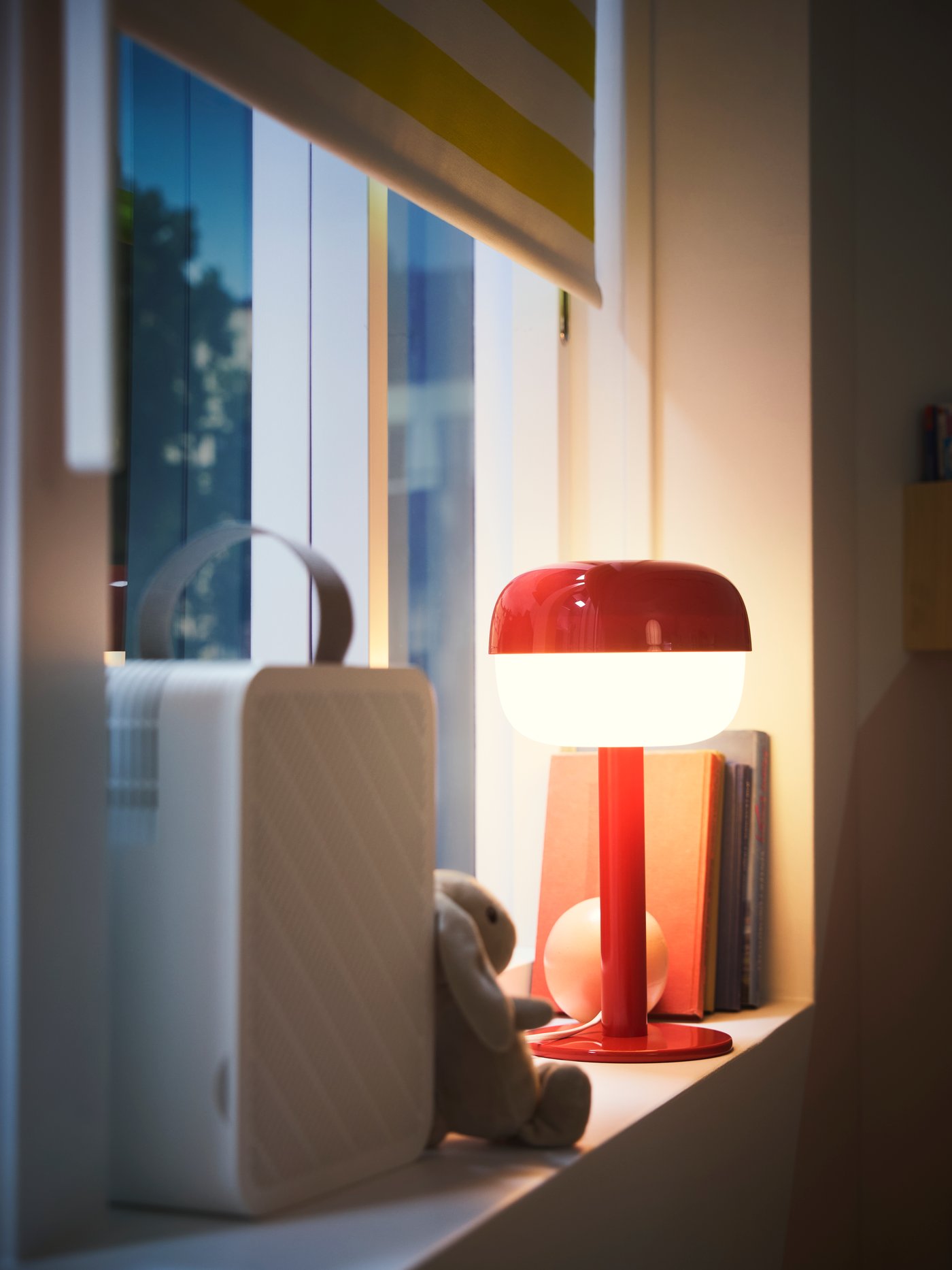 Close-up of window with a block-out roller blind, an UPPÅTVIND air-purifier and a table lamp standing on the window sill.