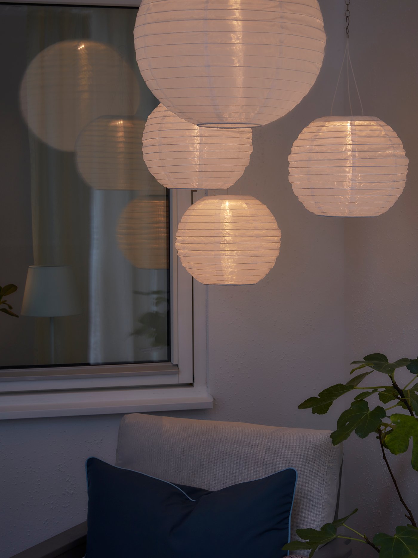 Four round, white solar-powered pendant lamps are creating cosy mood lighting in a darkened outdoor space.
