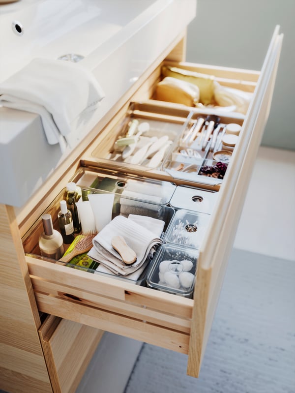 Wood cabinet underneath a white sink with one of the drawers open showing beauty products organized inside