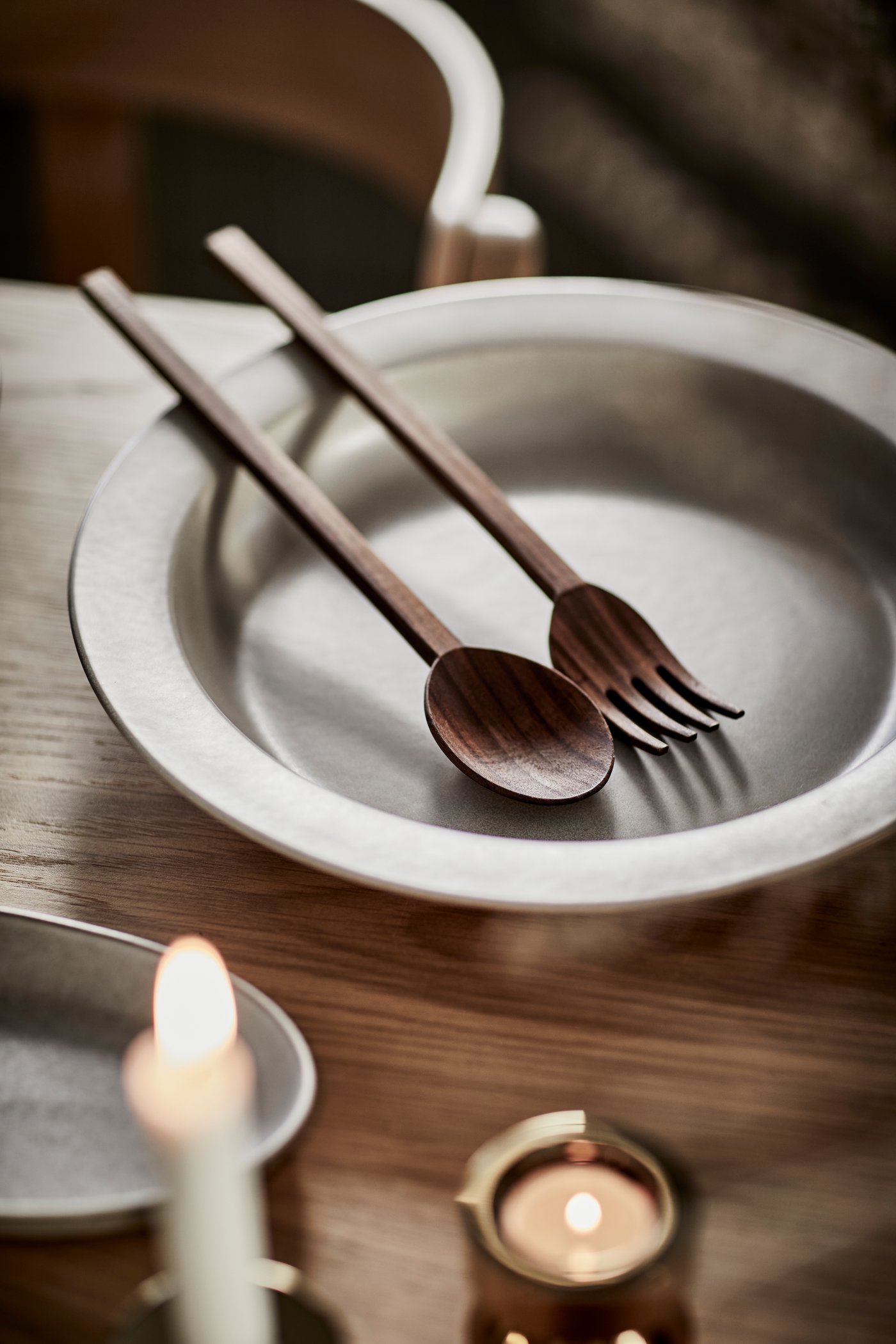 Una tavola con stoviglie della collezione STOCKHOLM 2025 e alcune candele accese. Dietro, una sedia STOCKHOLM 2025 in rovere con seduta in pelle.