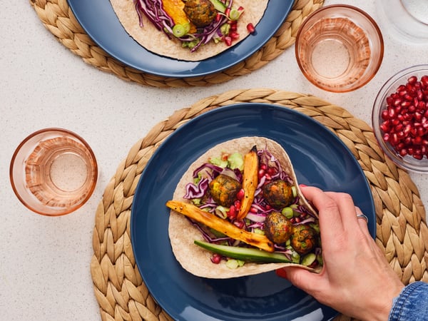 Detalle de una mano sujetando un taco mexicano sobre un plato color azul en un sobremantel.