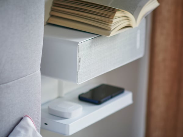 A white SYMFONISK bookshelf speaker mounted to a wall, functioning as a small bedside table.