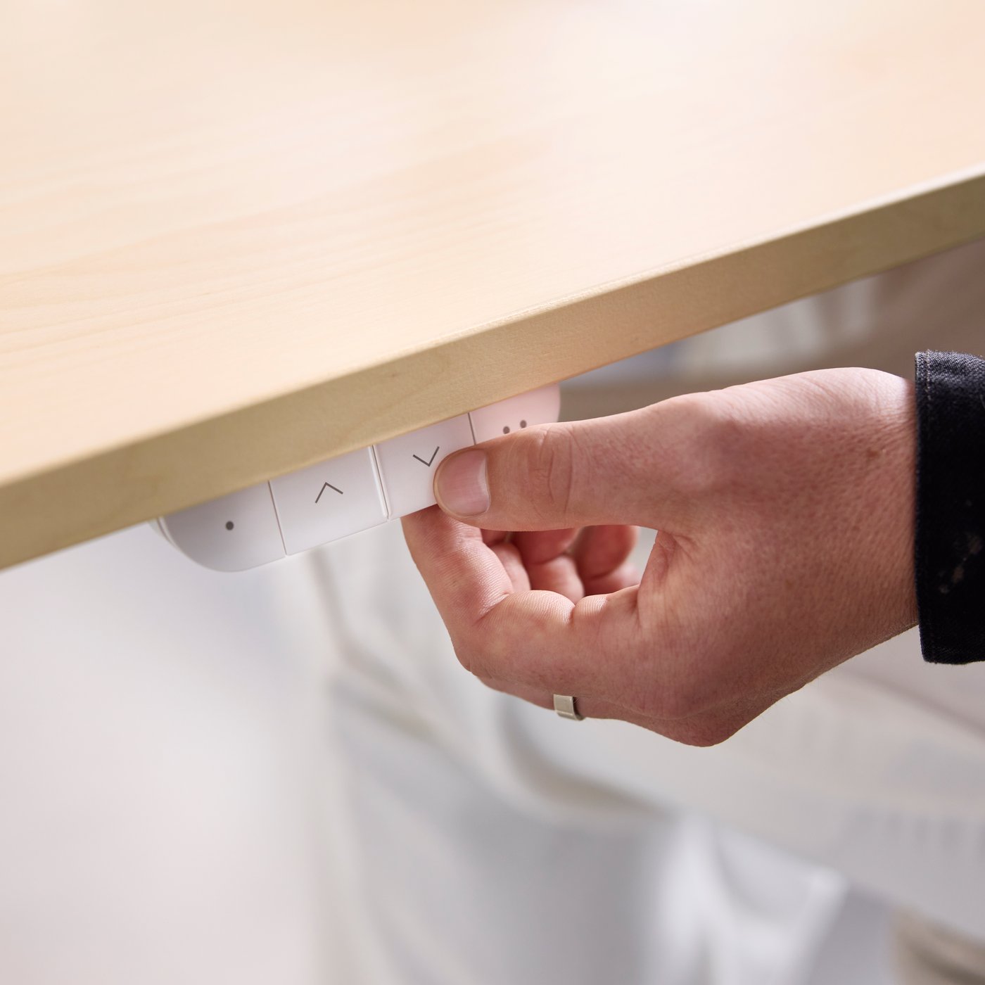 A close-up of a person’s hand pressing the buttons on a beige/white MITTZON frame with acoustic screen in an office setting.