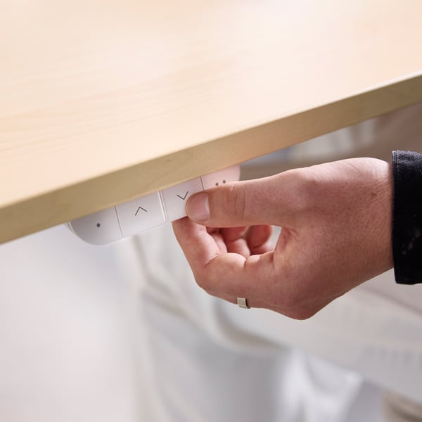 A close-up of a person’s hand pressing the buttons on a beige/white MITTZON frame with acoustic screen in an office setting.