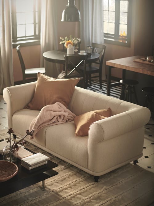 Modernes Wohnzimmer mit einem VISKAFORS 2er-Sofa, u. a. mit einem INGATORP Ausziehtisch, einem PEDERSBORG Teppich, einem TOFTERYD Couchtisch und einem STOCKHOLM Teppich. Auf dem Sofa sind ein Plaid und verschiedene Kissen zu sehen.