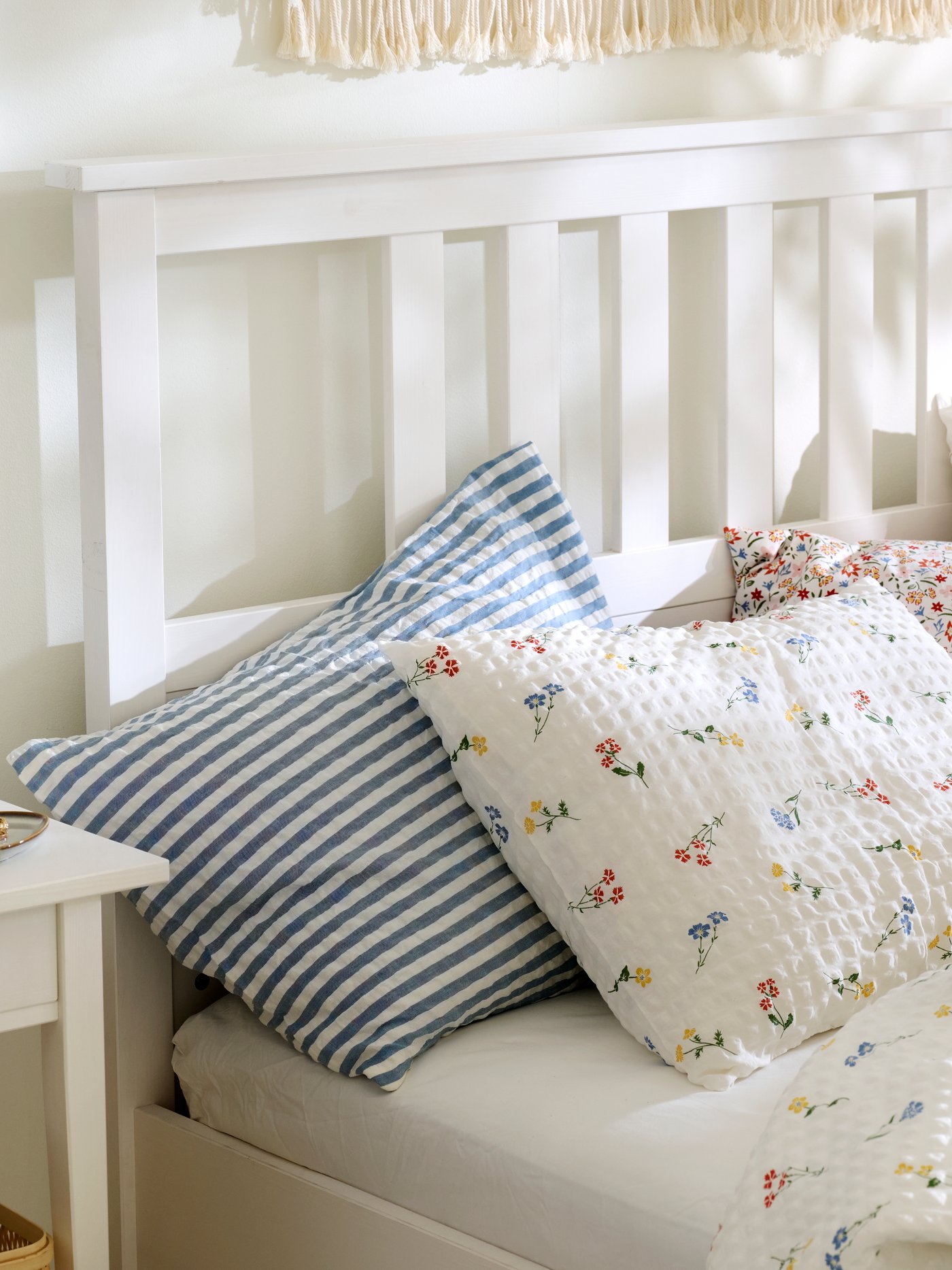 Close-up of a white HEMNES bed made with PILDVÄRGMAL duvet cover and pillowcases and bedding in other light colours.