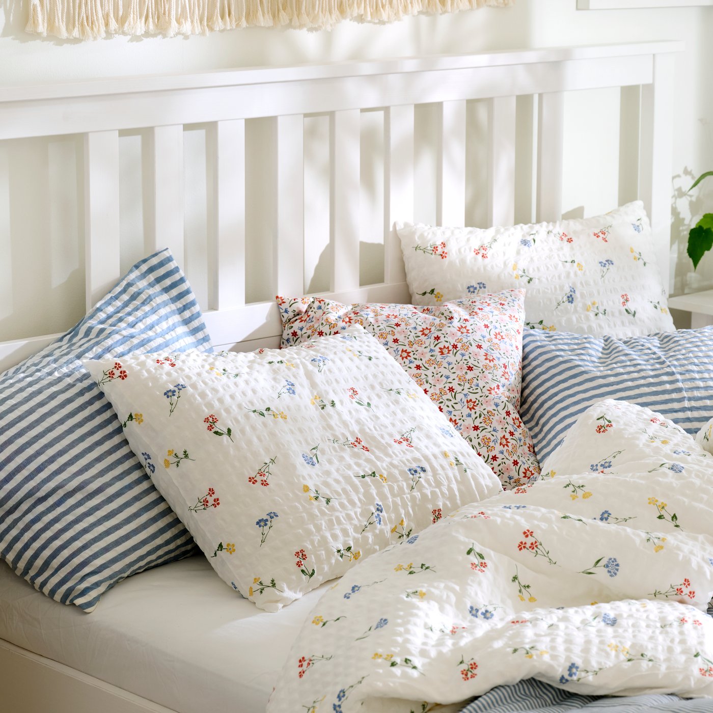 Close-up of a white HEMNES bed made with PILDVÄRGMAL duvet cover and pillowcases and bedding in other light colours.