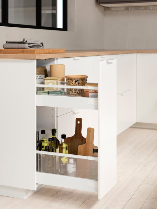 Eine Küche mit einem ausziehbaren METOD Unterschrank mit weißer VEDDINGE Front, der offen ist und Holzschneidebretter, Öle und Behälter zu zeigt.
