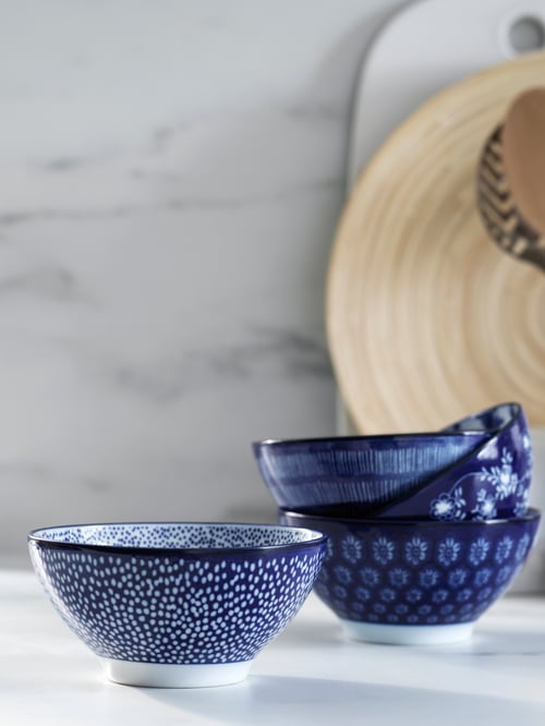 Quatre petits bols en porcelaine bleue à motifs différents sur un comptoir blanc avec un arrière-plan gris, devant des planches à découper.