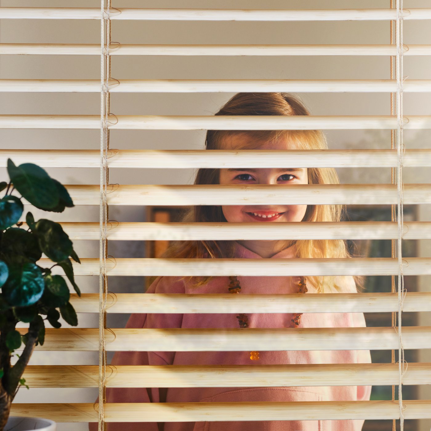 A close-up of a smiling child looking through a VECKLARFLY Venetian blind made from bamboo.