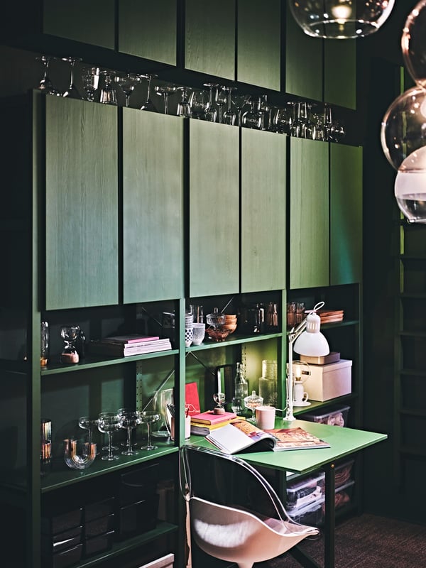 IVAR cabinets painted in green is placed against a wall, filled with tableware, wine glasses and storage boxes.