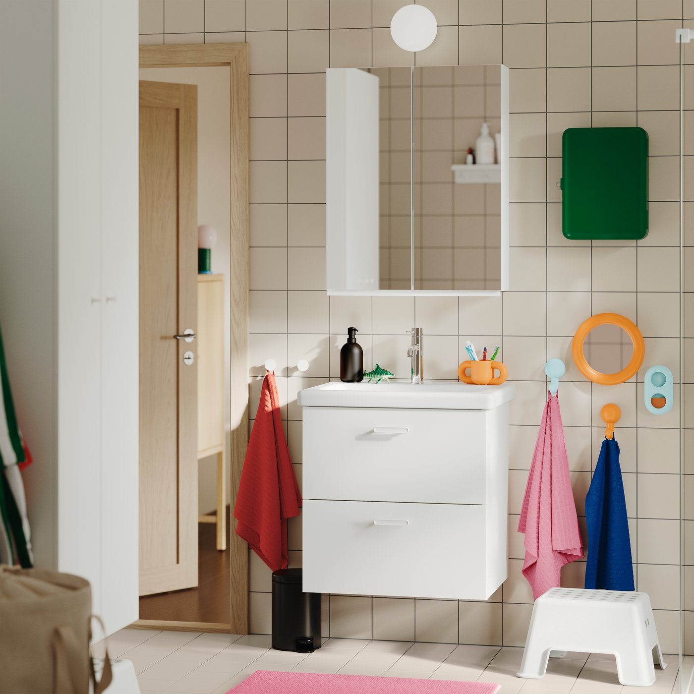 Ein gefliestes Badezimmer mit dem weißen TVÄLLEN/ENHET Waschbeckenunterschrank mit zwei Schubladen, wandmontiert und mit bunten Handtüchern in der Nähe.