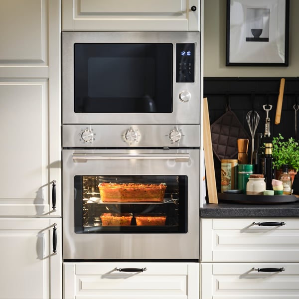 Ein STENABY Heißluftofen und eine Einbau-Mikrowelle, beide aus Edelstahl, sind in einer Küche mit cremefarbenen BODBYN-Fronten untergebracht.