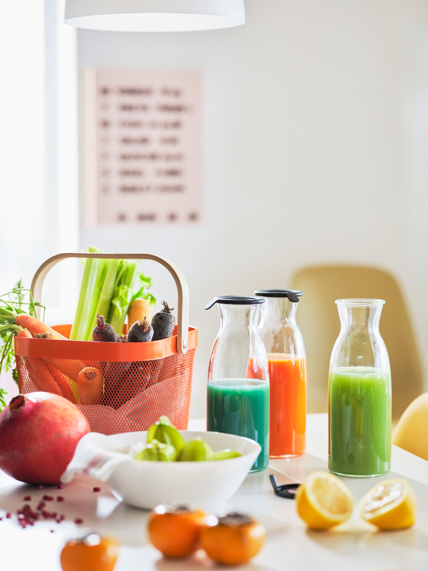 A white tabletop with a RISATORP basket and a colour-bursting mix of vegetables, fruits and juices in clear-glass carafes.