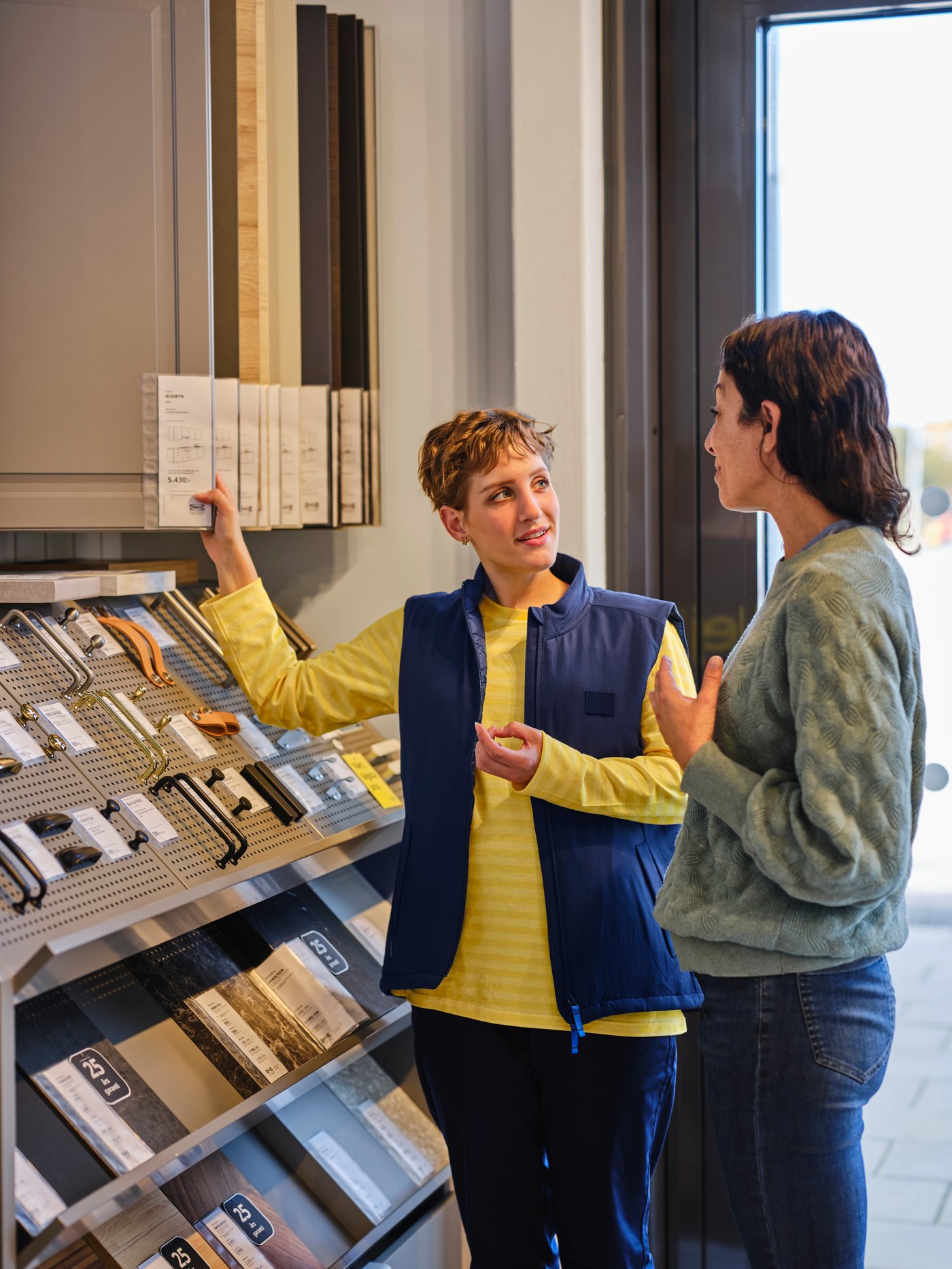 An IKEA co-worker is showing kitchen door fronts to a customer.