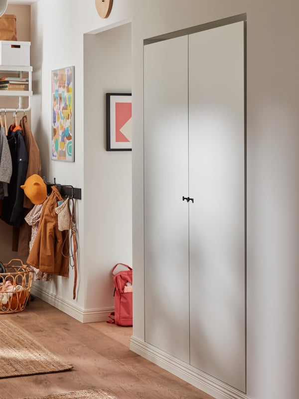 A white wardrobe combination retrofitted on an odd closet niche in the hallway, wooden floors, a red backpack.