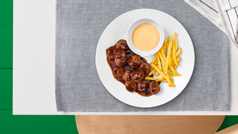 Ein Teller mit Plantbullarn, Pommes und einem Schälchen Dip stehen auf einem grauen Platzset.