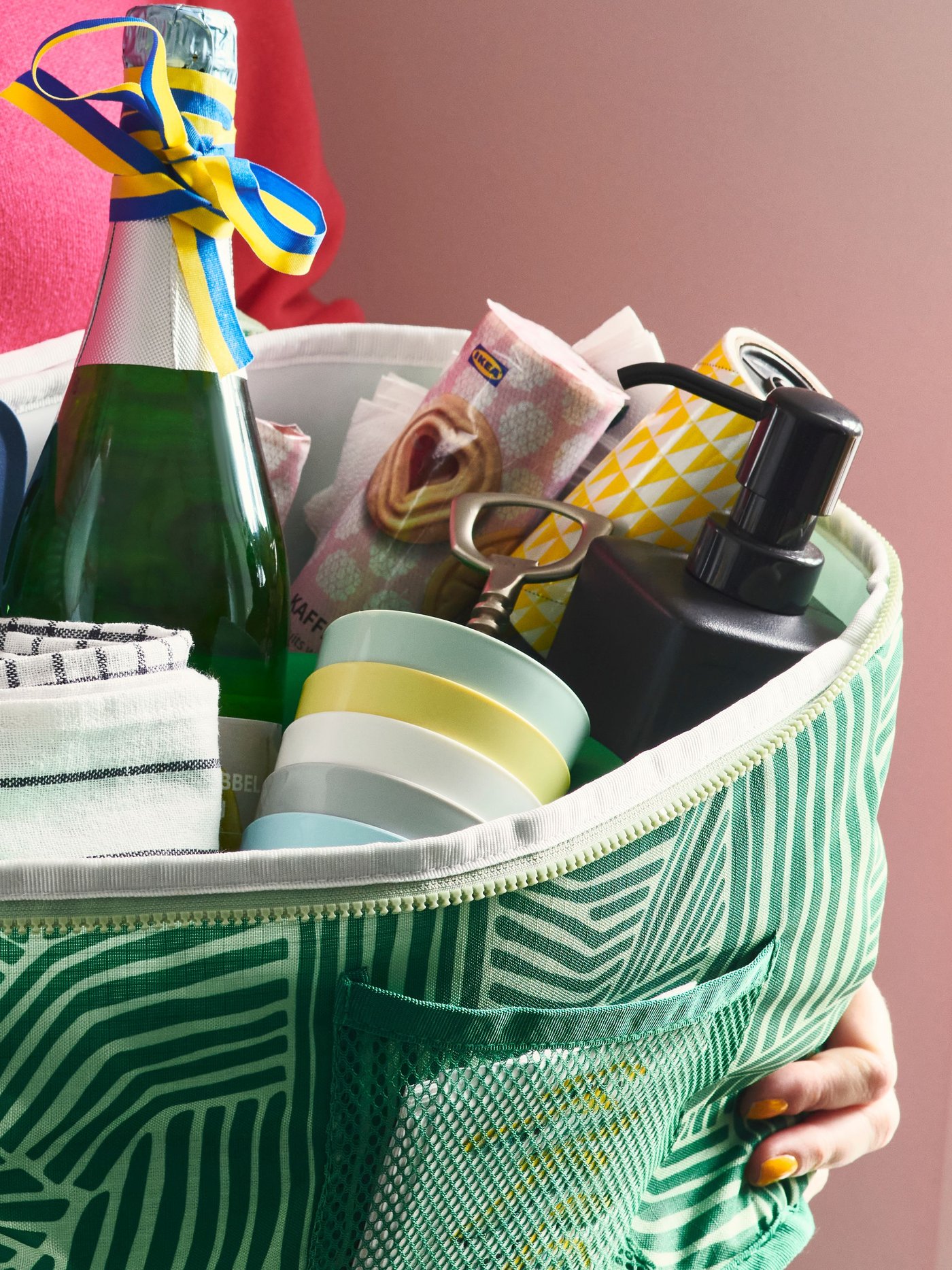 En person håller i en NÄBBFISK kylväska som innehåller bland annat pärondricka, muggar, diskborste och diskhandduk.