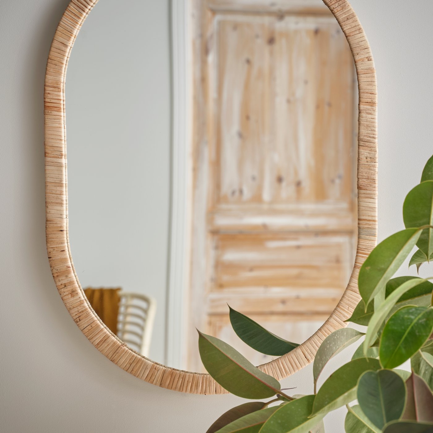 A large mirror with a wooden frame hangs on the wall. In front of a plant. 