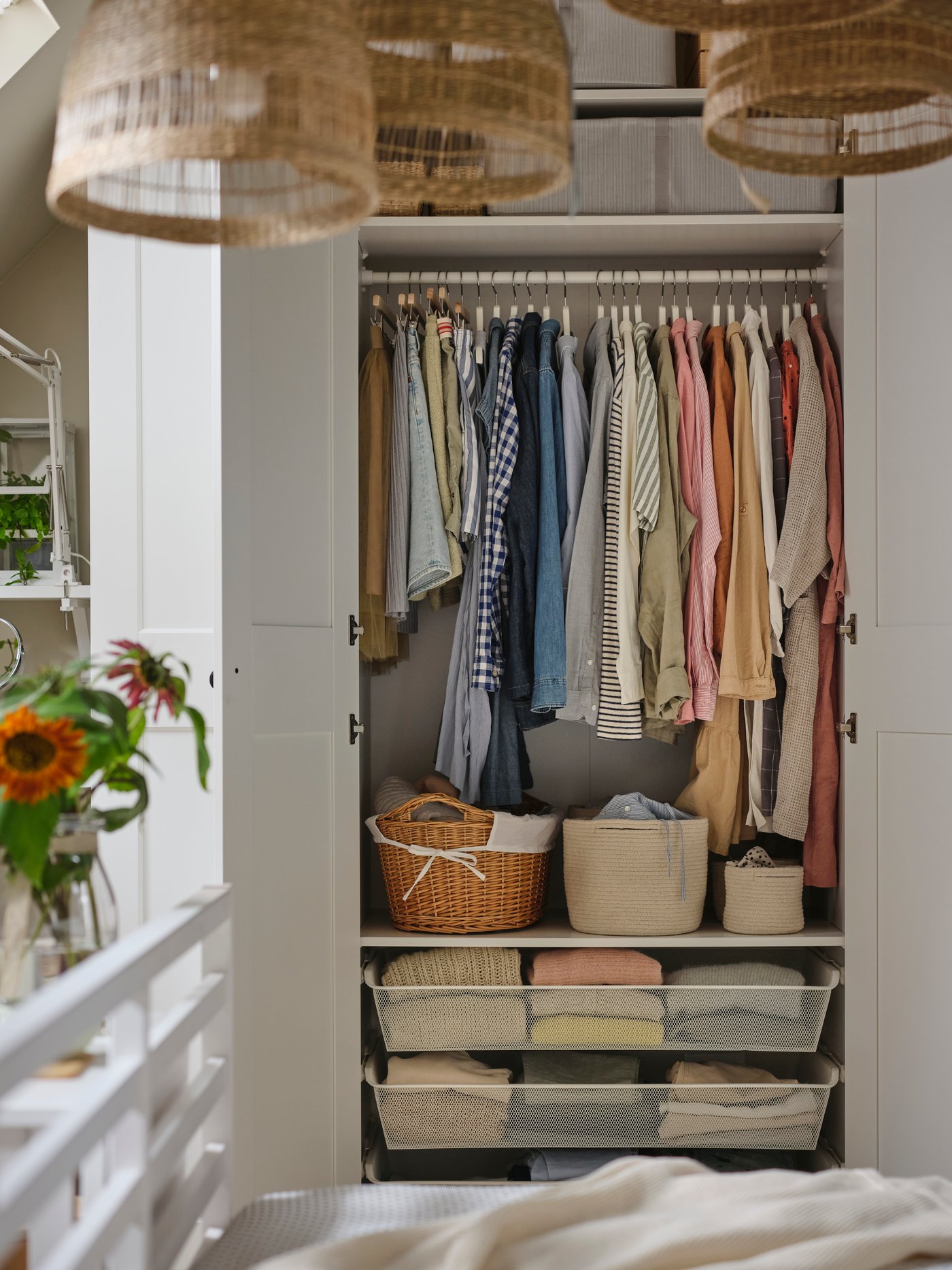 Biała szafa PAX GRIMO z dwoma otwartymi drzwiami, w której widoczne są ubrania na drążkach, w szufladach z siatki i w koszach na półkach.