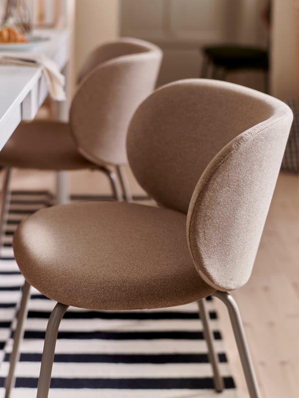 Two dark beige KRYLBO chairs stand at a white EKEDALEN extendable table on a striped flatwoven STOCKHOLM rug.