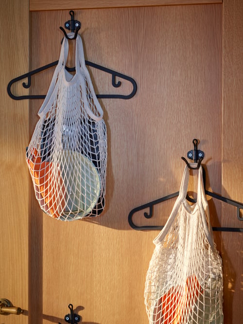 The inside of a wooden front door with two double scattered hooks, where each one has a hanger and a cotton KUNGFORS net bag.