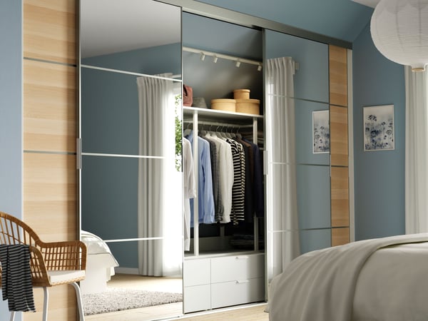 A SKYTTA sliding door solution in a bright bedroom. The doors are partly open, showing clothes and storage behind.