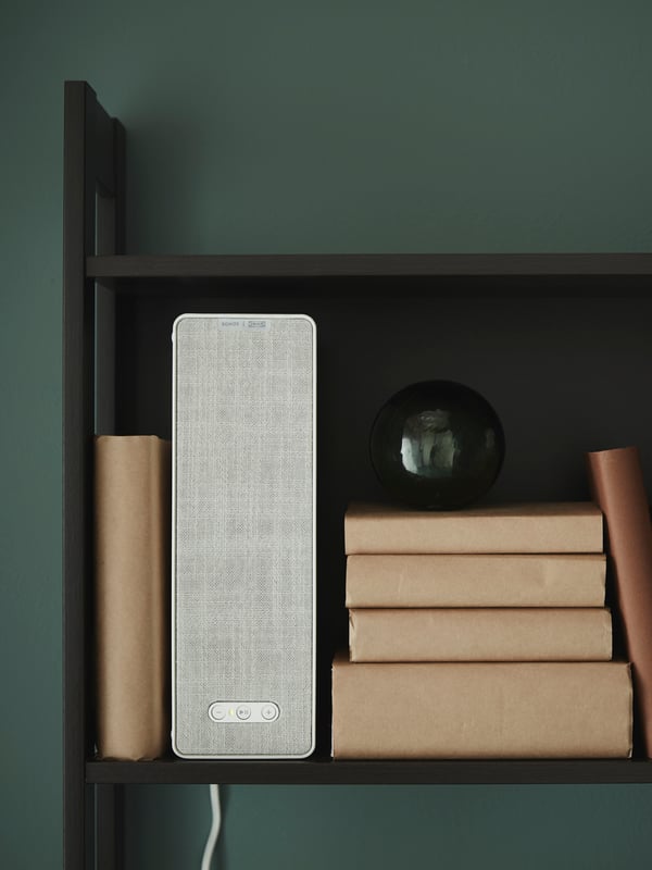 מנורה עם רמקול Wi-Fi SYMFONISK לצד אביזרים דקורטיביים על ארון הניצב בפינת אוכל.