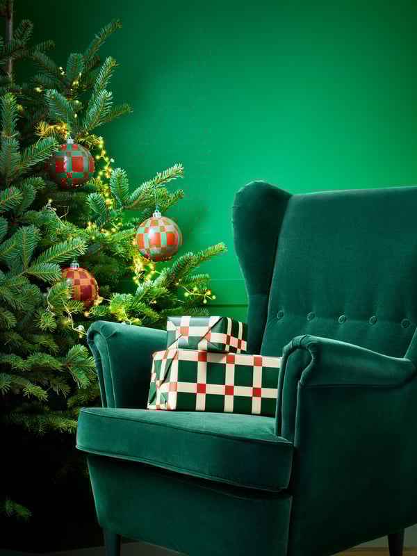 En grön STRANDMON sammetsfåtölj intill en julgran i ett grönt rum.