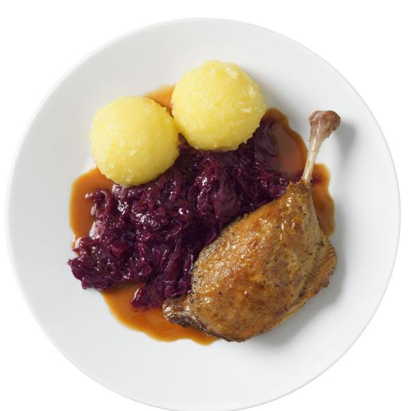 Ein Teller mit einer Entenkeule, 2 Kartoffelknödel, Rotkohl und brauner Soße.