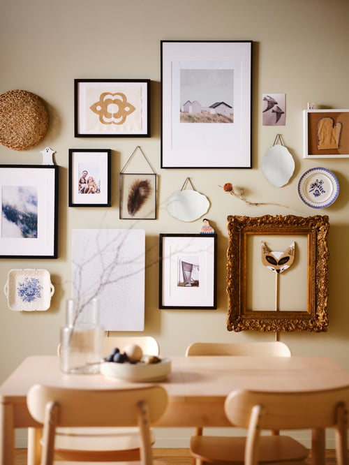 Dining area featuring multiple black frames containing pictures mounted to a wall. An extendable table is in the foreground.