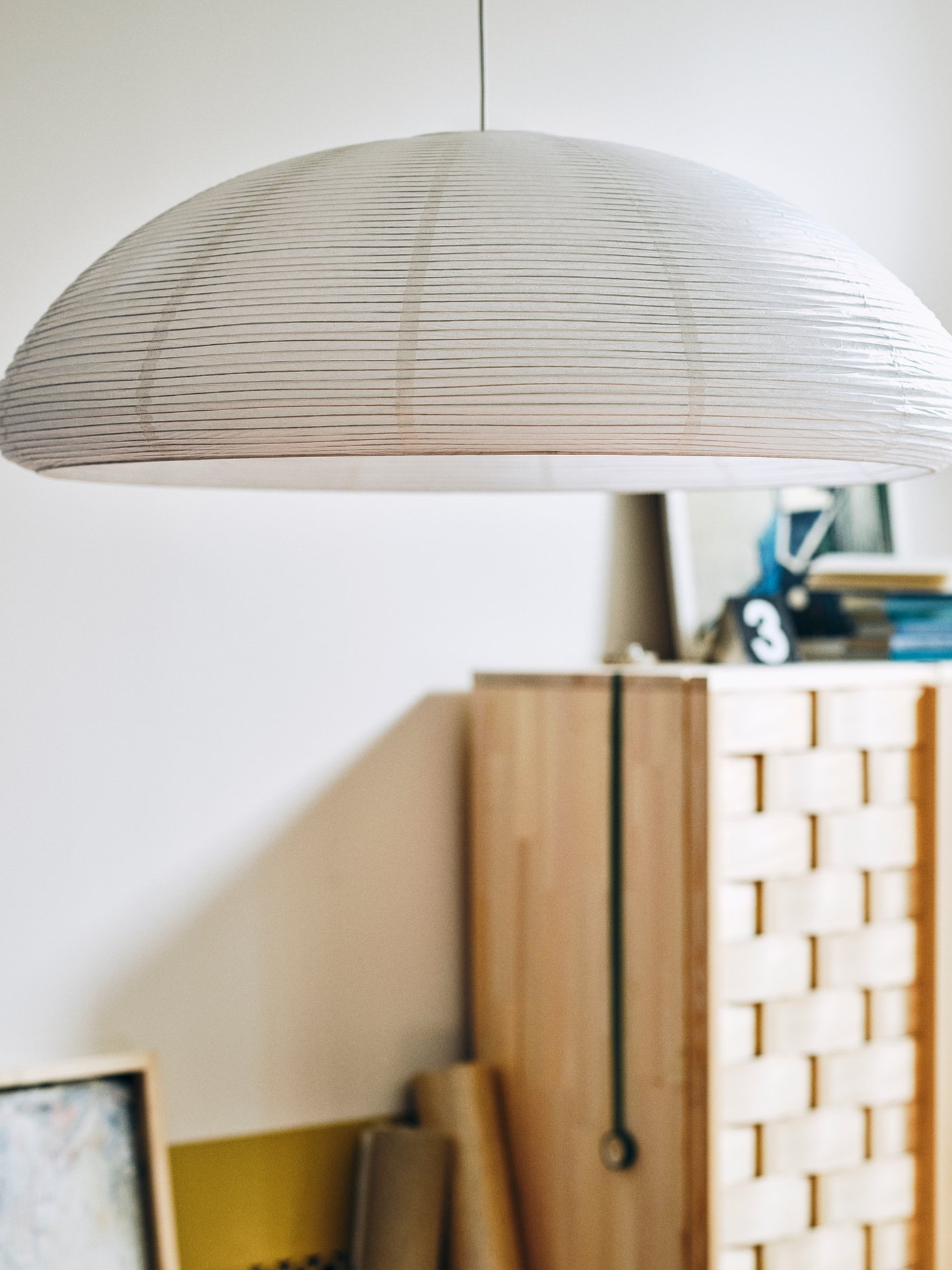 A white, dome-shaped IKEA PS 2026 ceiling lamp with a textured surface hangs in a bright room, with a woven wooden cabinet in the background.