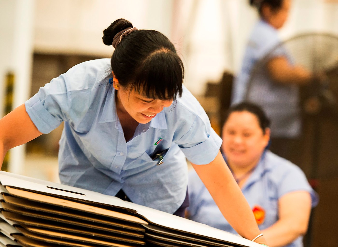 Arbetare i blå skjortor hanterar kartonger i en fabriksmiljö.
