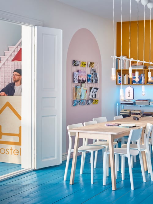 Dining area with a white dining table, white chairs, a wall mounted unit, a memo board, a shelving unit, white pendant lamps.