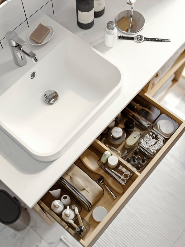 Tiroir supérieur d’un meuble-lavabo ouvert, révélant des accessoires de rangement pour tiroir VISSLAÅN brun-beige contenant des produits de soins personnels.