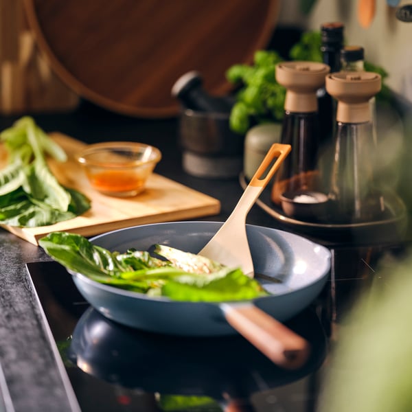 Une spatule KNORRHANE pour remuer les légumes à feuilles dans une poêle sur la cuisinière.